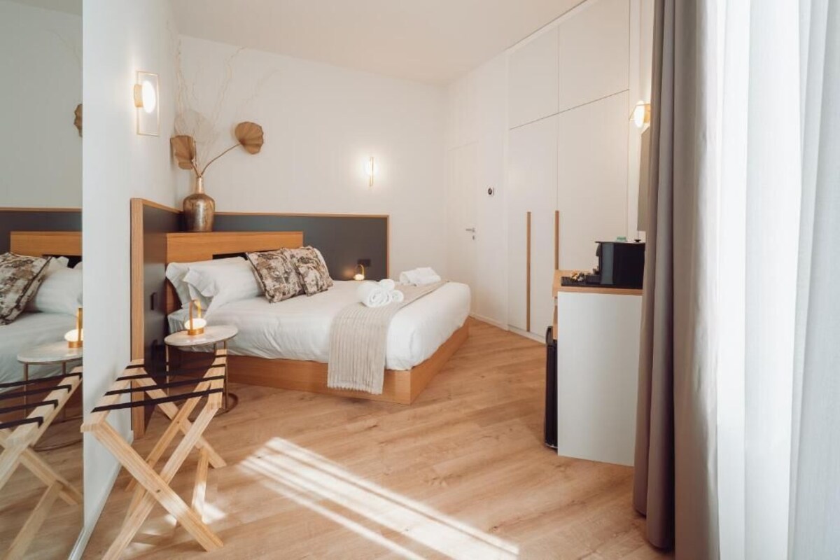 Un dormitorio moderno con una cama de madera, mesitas de noche, una mesita auxiliar, un espejo y una lámpara de pared.