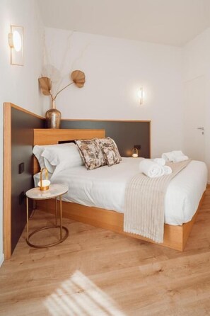 Un dormitorio ordenado con una cama de madera, mesitas de noche y un jarrón con ramas secas.