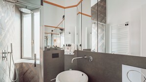 A modern bathroom with a large mirror, a white sink, and a shower area. - ARCASuite Trevi (Rome)