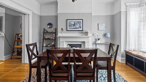 A dining area with a wooden table and chairs, a chandelier, a fireplace, and a bookshelf.