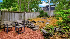 A backyard with a wooden fence, a bench, a table, and a garden with rocks and plants.