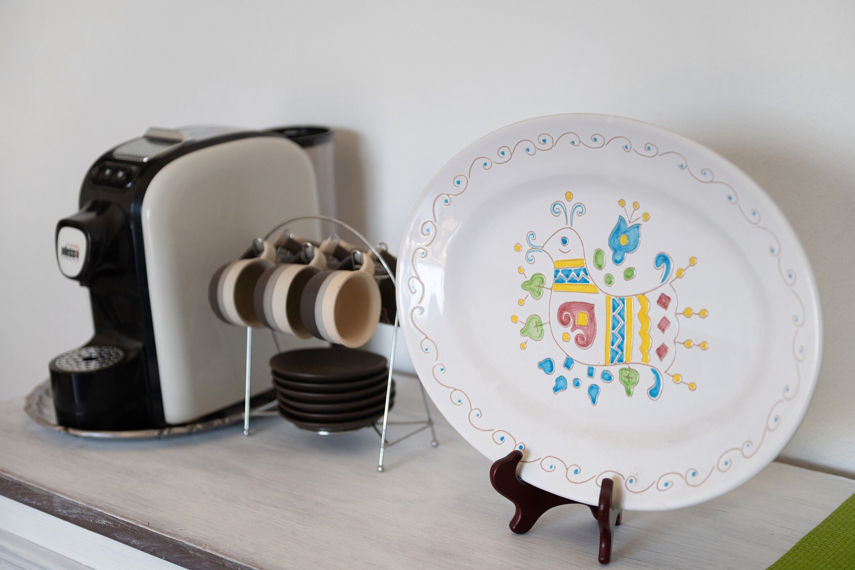 A coffee maker, a plate with a colorful design, and a stack of plates on a shelf.