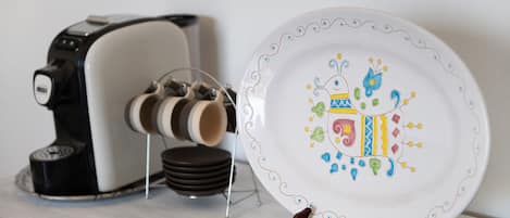 A coffee maker, a plate with a colorful design, and a stack of plates on a shelf.