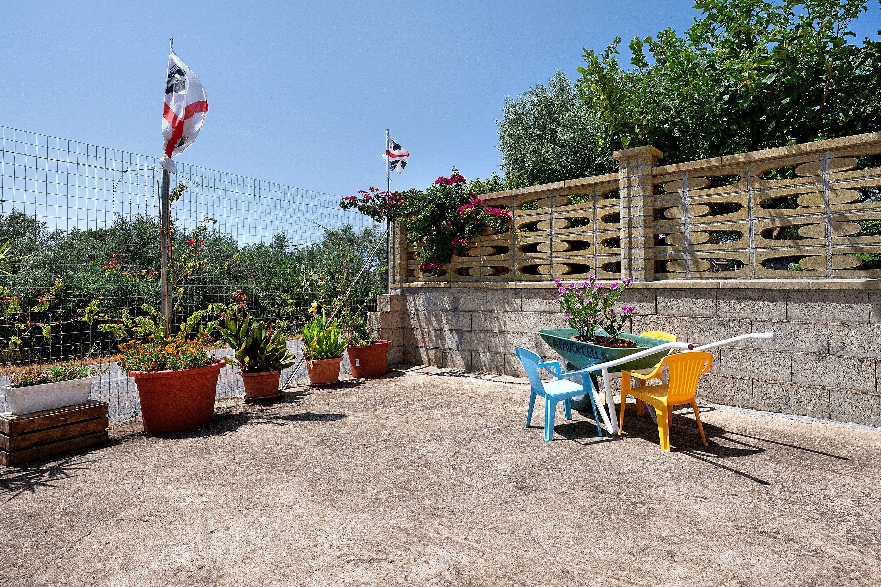 An outdoor patio area with a table and chairs, potted plants, and a stone wall.