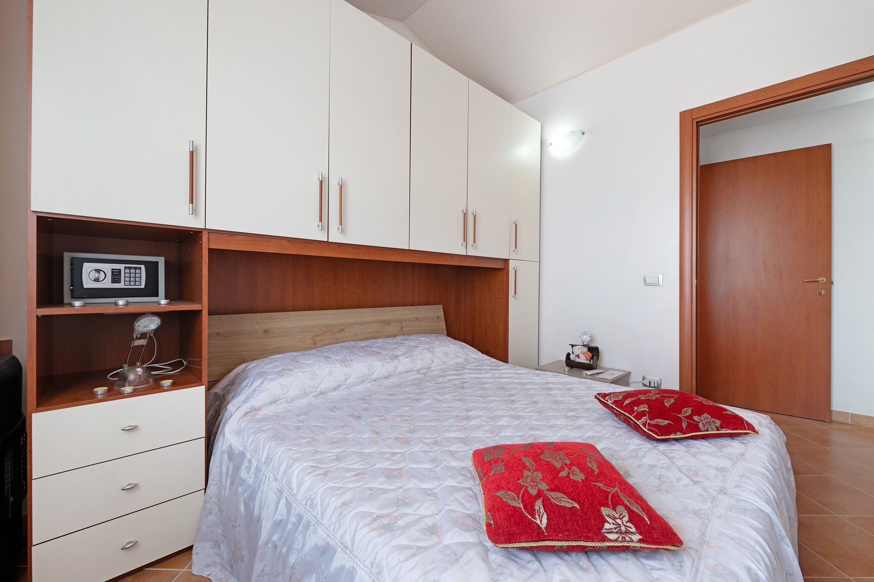 A bedroom with a bed, a wardrobe, a bedside table, and a door.