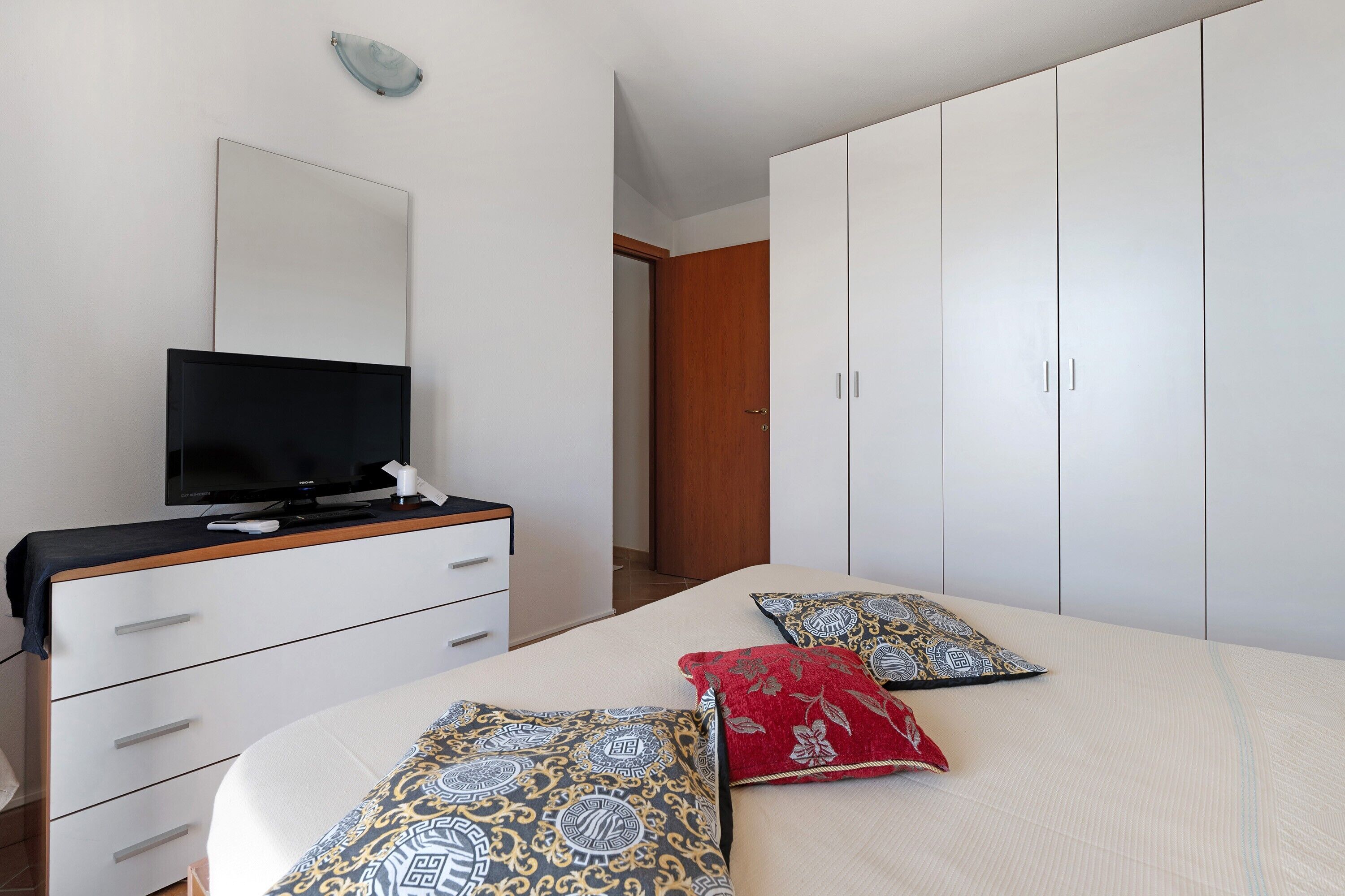 Een slaapkamer met een bed, een televisie op een dressoir en een kledingkast.