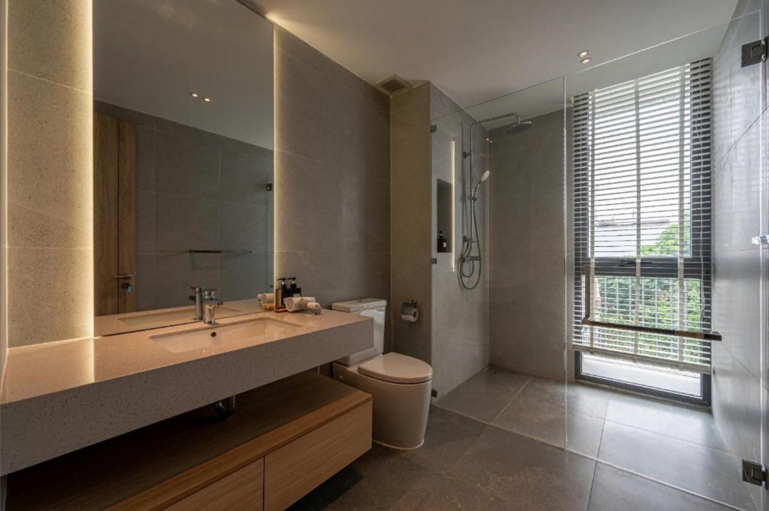 A modern bathroom with a large mirror, a sink, a toilet, and a shower.