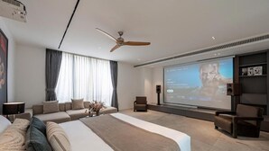 Una camera d'albergo moderna con un letto grande, un'area salotto, una ventola a soffitto, uno schermo per proiettore e una televisione.