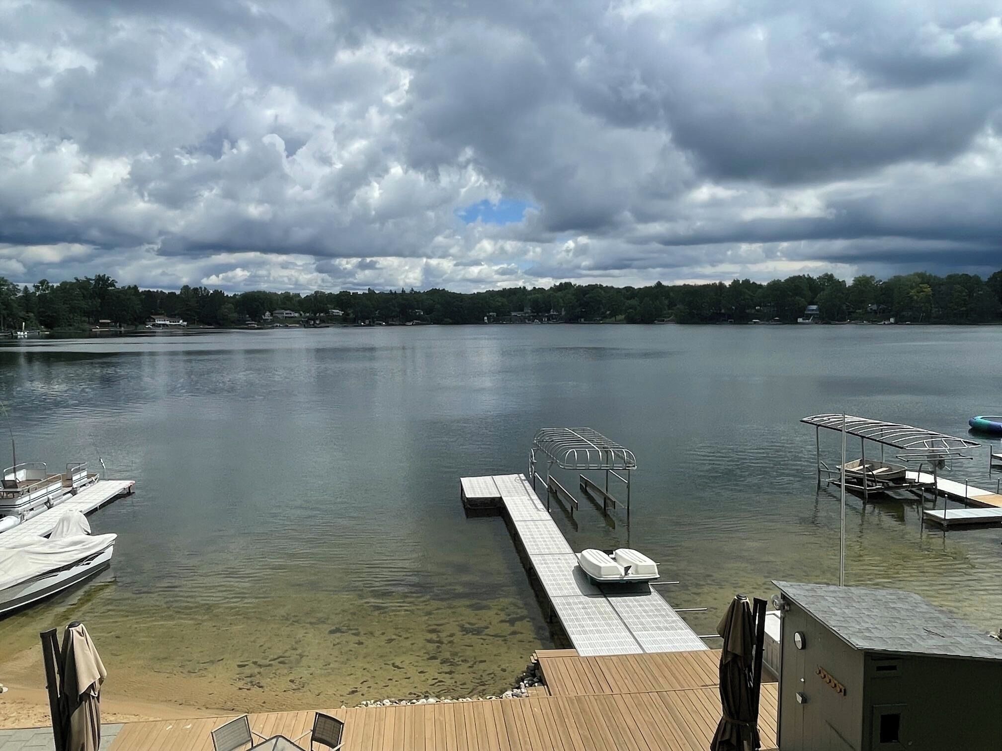 A lake with a dock, a covered seating area, and a small building.