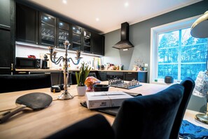 A modern kitchen with dark cabinets, a chessboard, and a large window with a view of trees. - Newly built single-family home with its own spa area (Telemark)