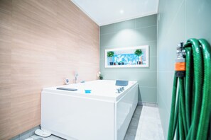 A modern bathroom with a freestanding bathtub, a wall-mounted shelf with plants, and a green hose. - Newly built single-family home with its own spa area (Telemark)