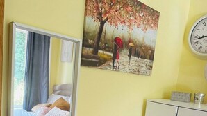 Ett rum med en säng, ett skrivbord, en stol, en spegel, en tavla, en klocka och ett skåp.