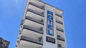 Un hotel de varios pisos con un llamativo letrero que dice 'HOTEL', unidades de aire acondicionado en los balcones y un número de contacto para reservas.
