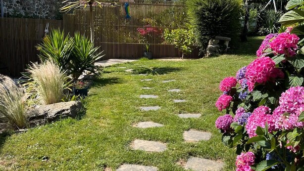 Un camí de pedra que serpenteja per un jardí ben cuidat, ple de flors d'hortènsia i diverses plantes.