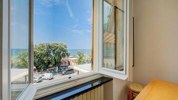 Una habitación con vistas a la calle y árboles, una ventana, un radiador y una pequeña mesa de madera.