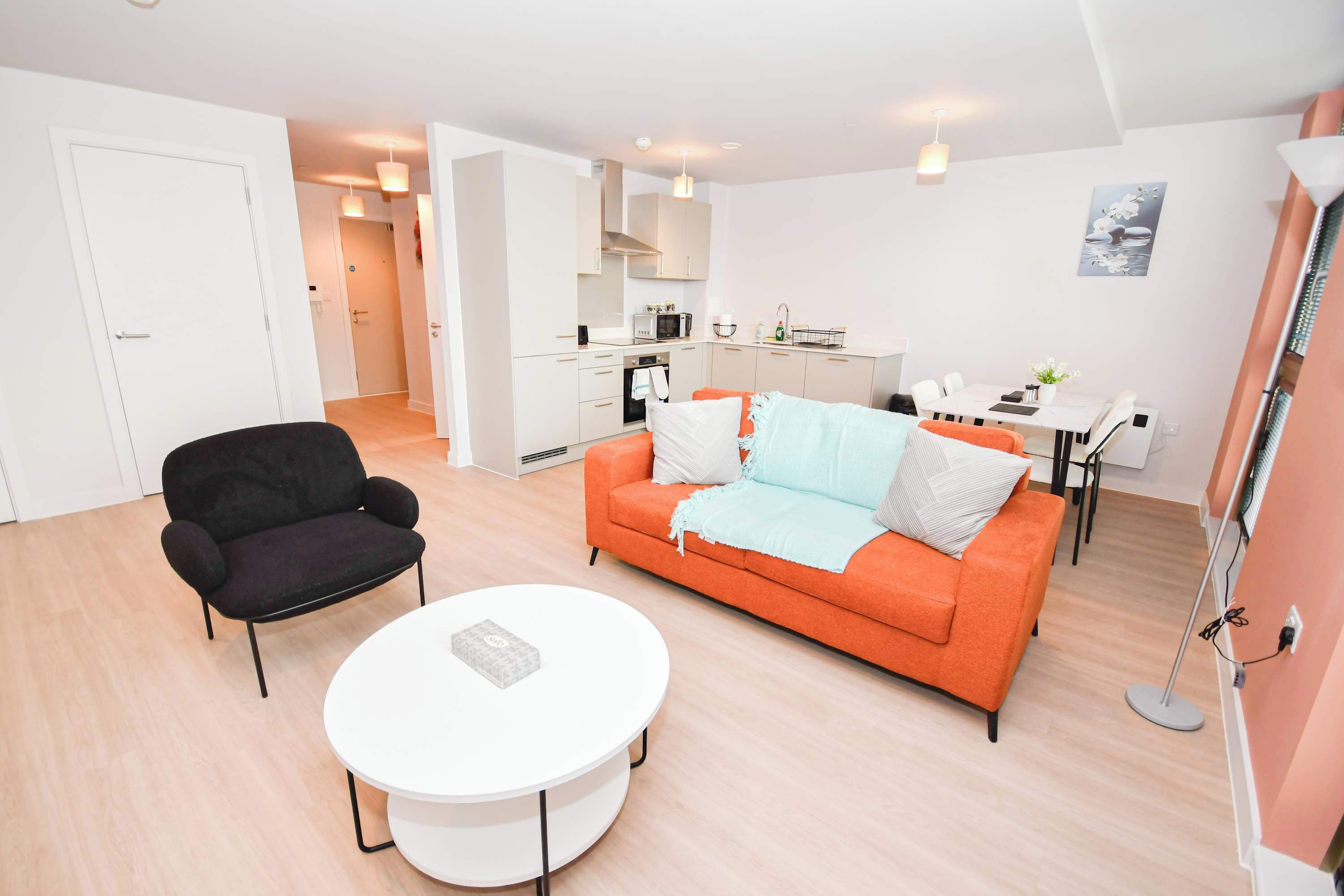 A modern living room with a sofa, a black armchair, a white coffee table, and a kitchen area in the background.
