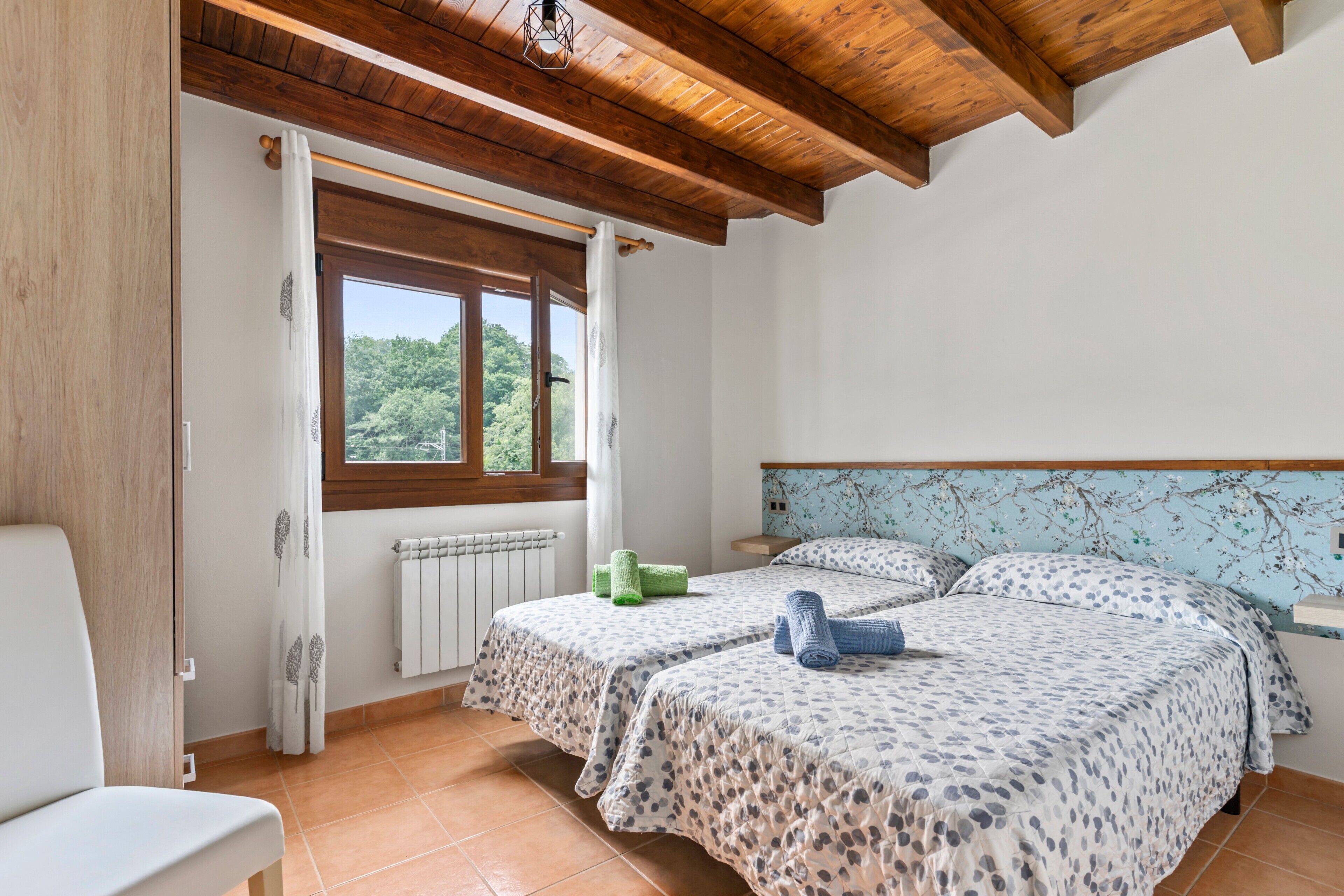 Ein Schlafzimmer mit zwei Betten, einem Fenster, einer Heizung und einer Holzbalkendecke.