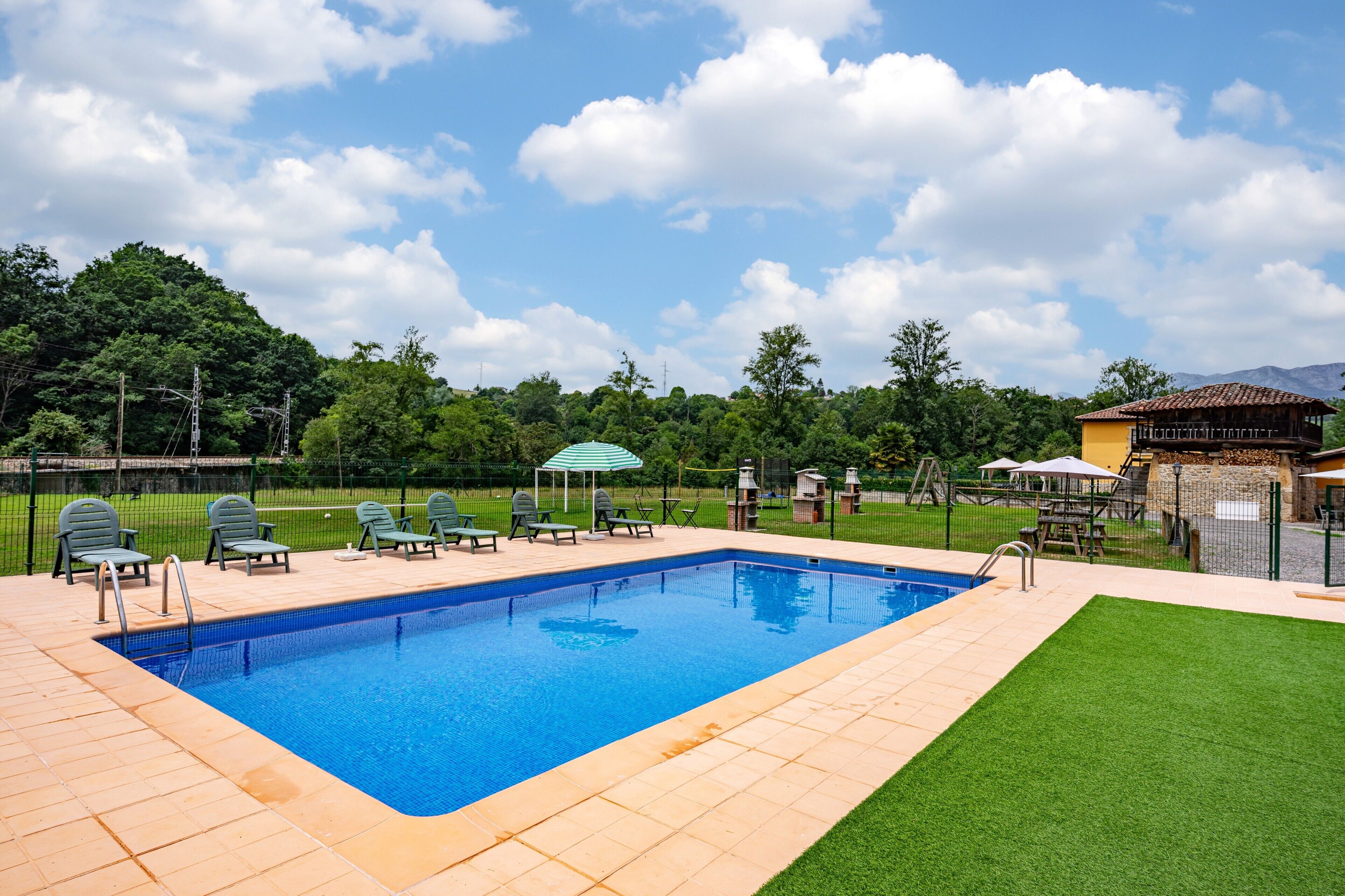 Una piscina rectangular con borde de baldosas, rodeada de césped y una valla.