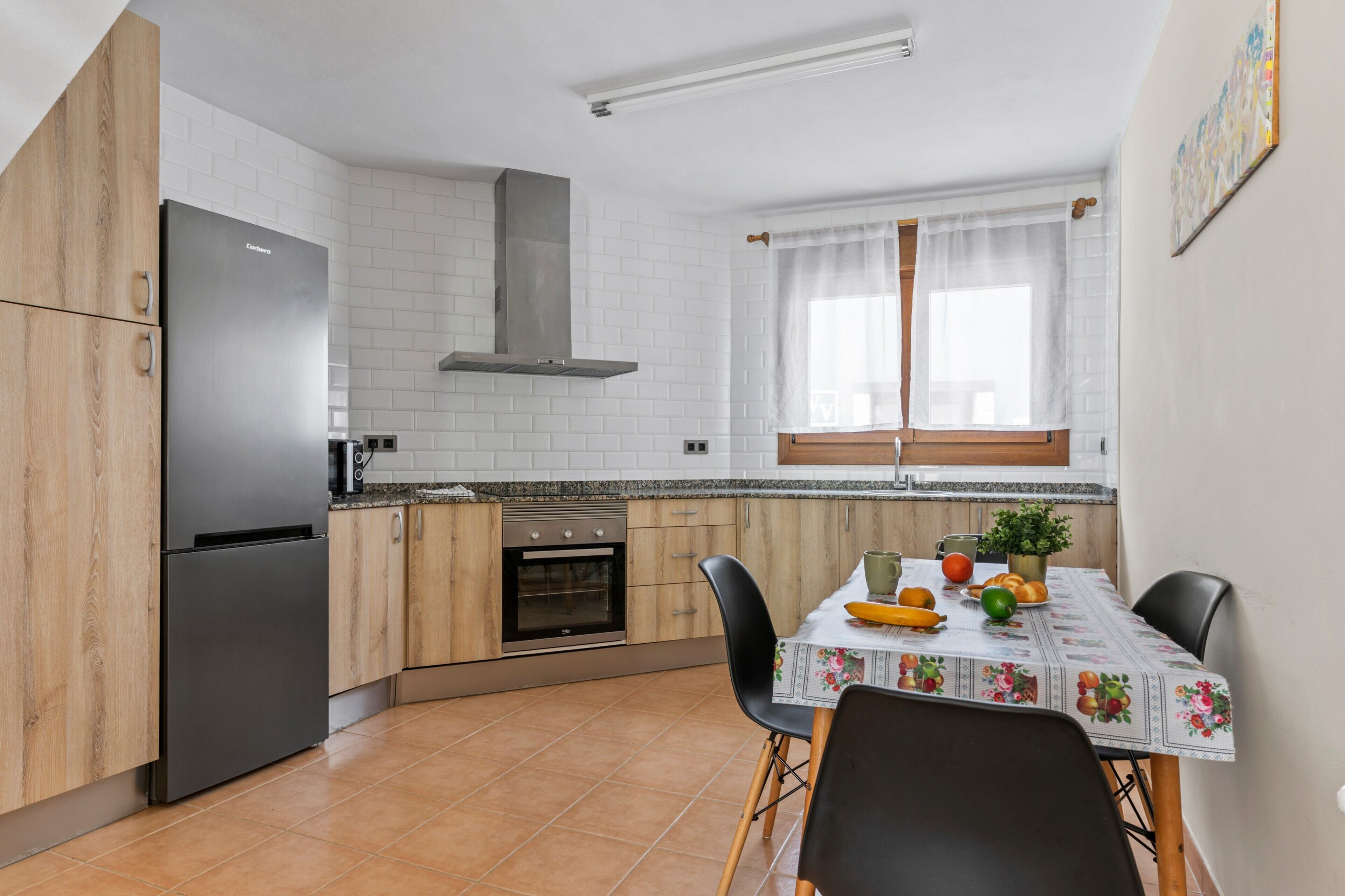 Cuina amb nevera, forn i taula de menjador amb cadires.