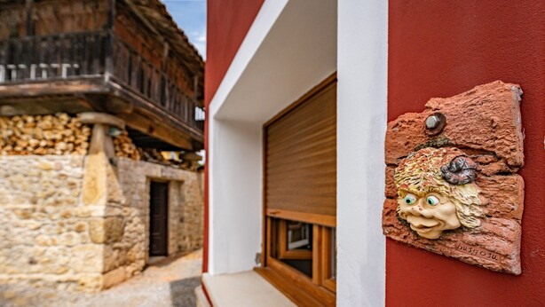 A narrow alleyway with a stone building on one side and a modern building with a wooden bench and a decorative wall plaque on the other.
