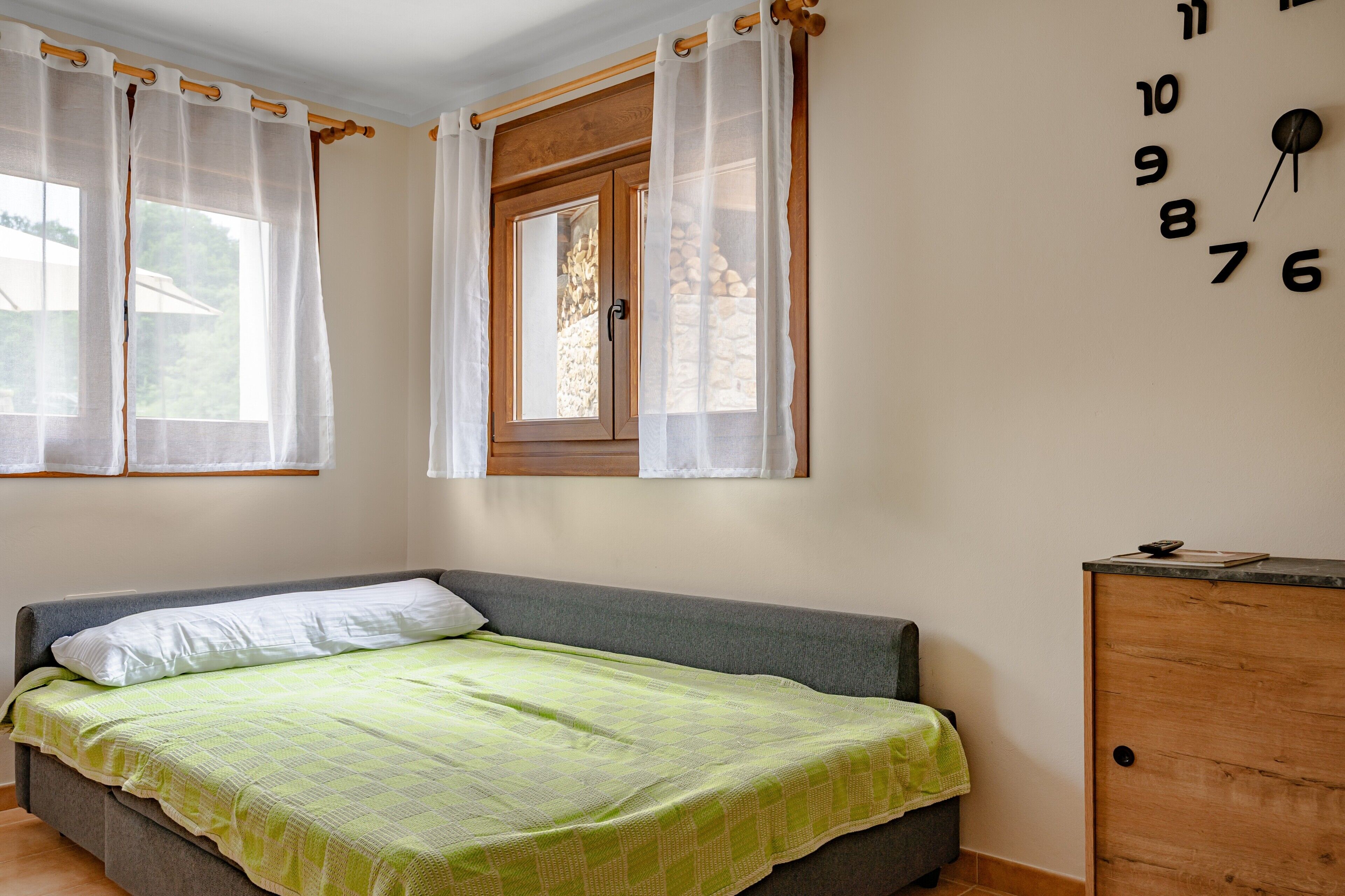 Un dormitorio con una cama, una ventana con cortinas, un armario de madera y un reloj de pared.