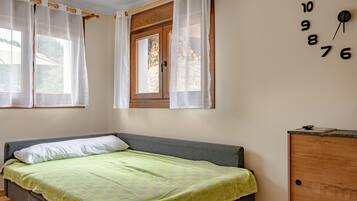 Un dormitorio con una cama, una ventana con cortinas, un armario de madera y un reloj de pared.