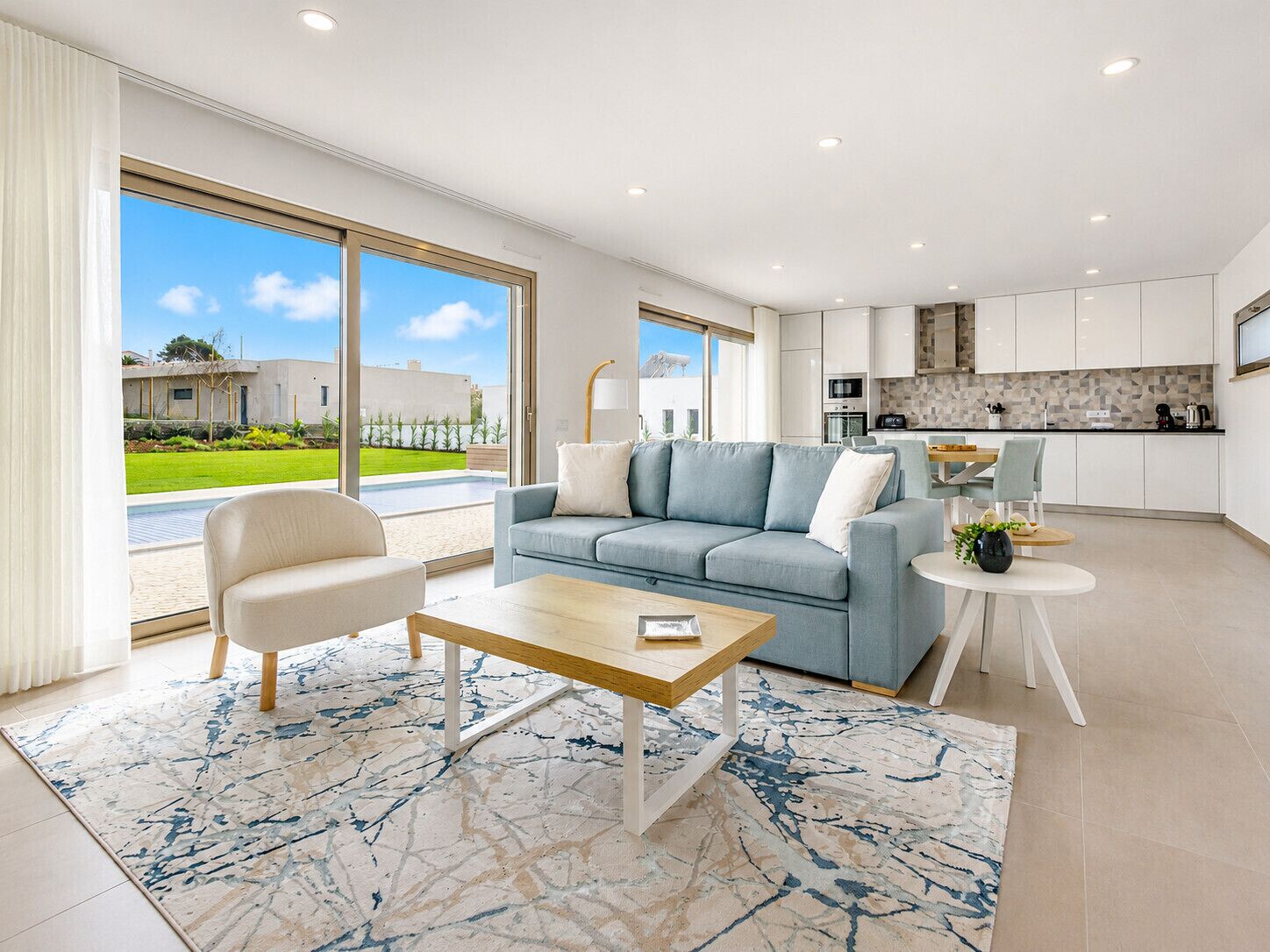 A modern living room with a sofa, armchair, coffee table, and a view of the outdoor garden.