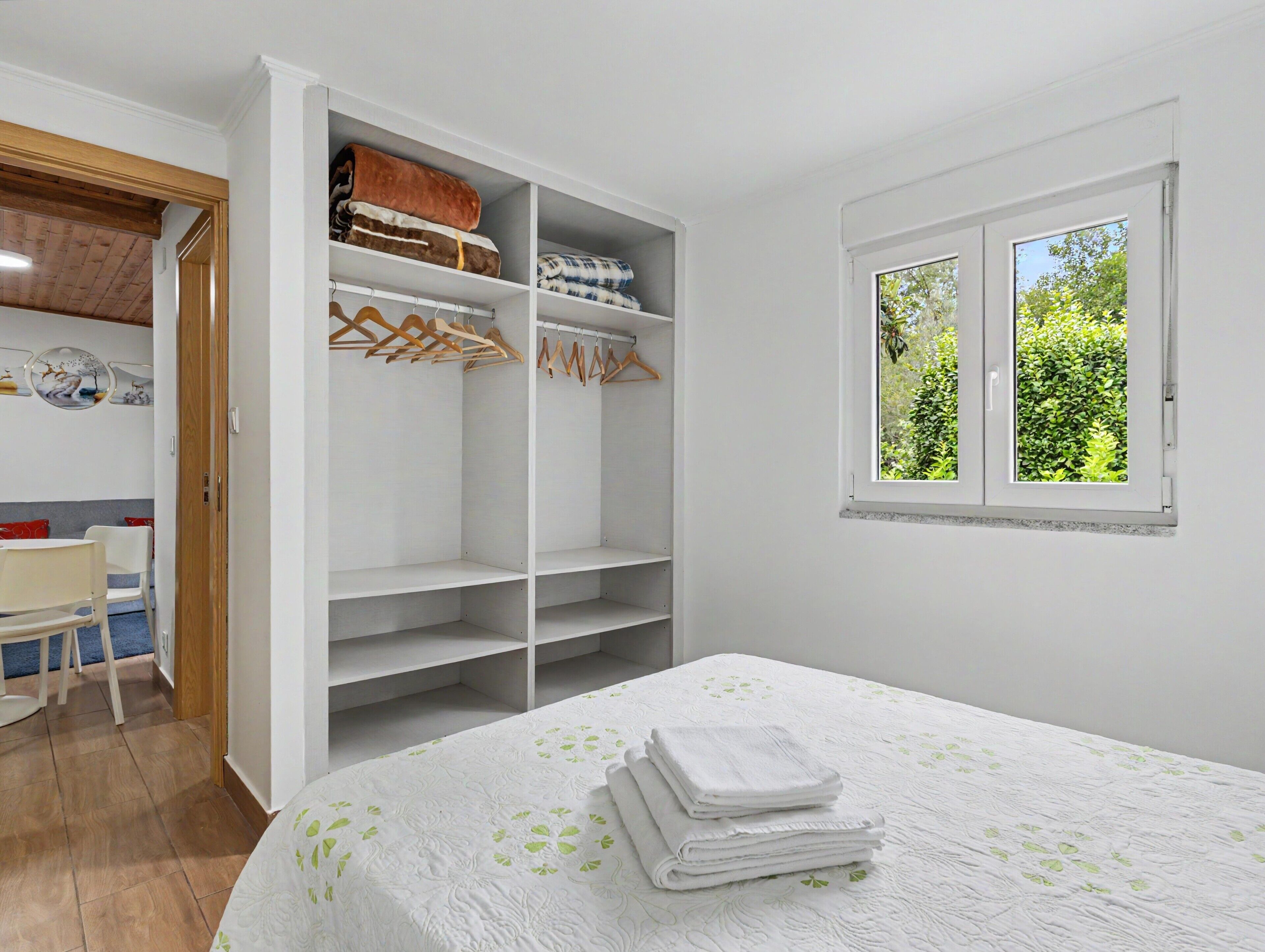 Ein Schlafzimmer mit einem Bett, einem Kleiderschrank, einem Fenster und einer Tür zu einem anderen Raum.
