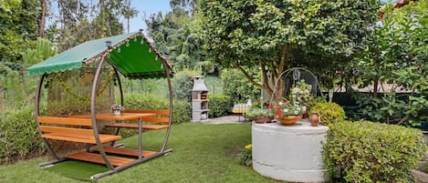 A garden with a wooden swing, a barbecue grill, and a variety of potted plants.