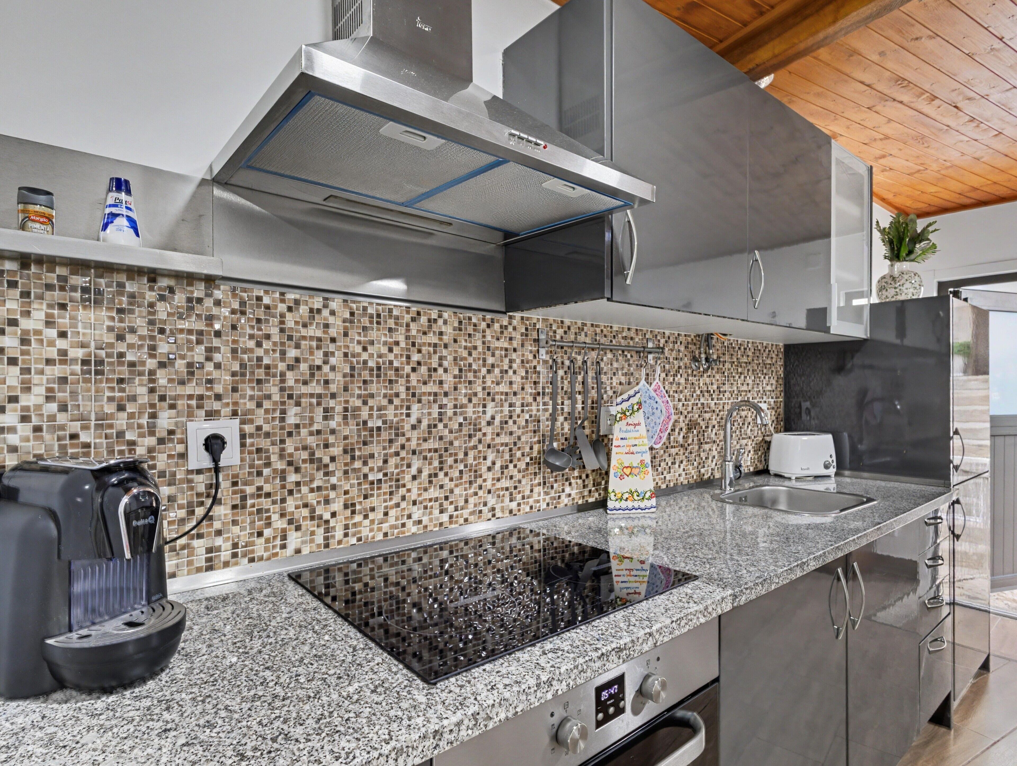 Eine moderne Küche mit Granitarbeitsplatte, Edelstahlgeräten und einer Rückwand mit Mosaikfliesen.