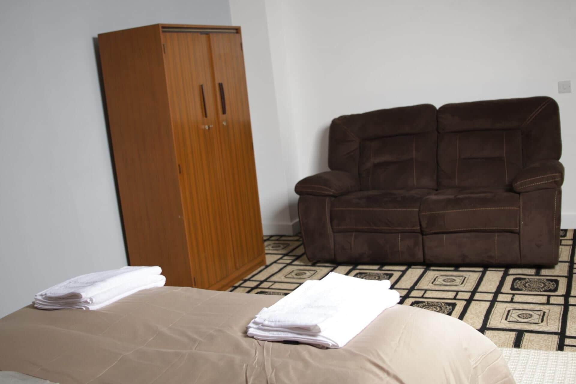 A room with a bed, a brown reclining chair, and a wooden wardrobe.