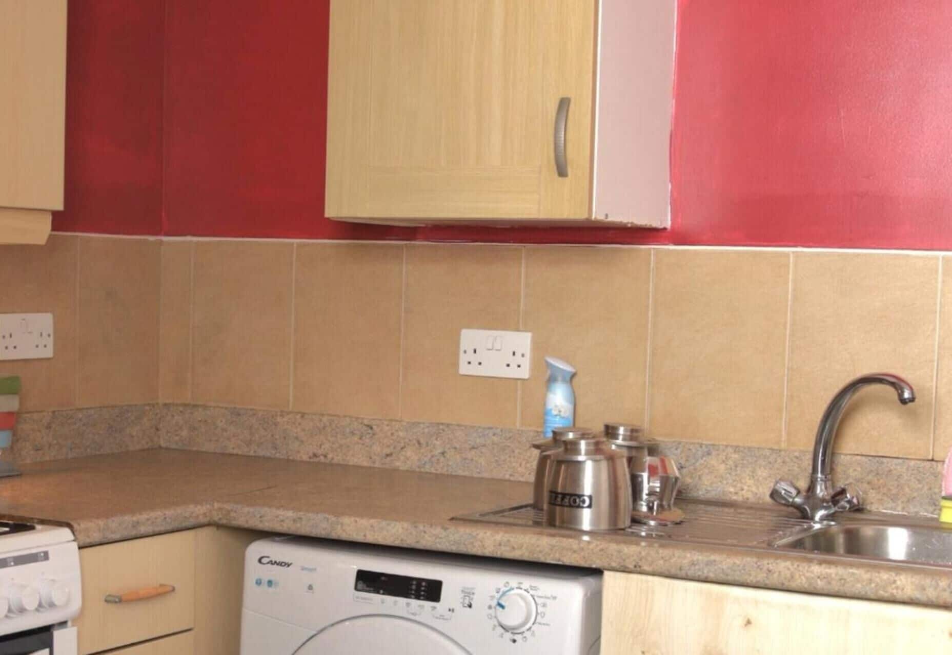 A kitchen with a washing machine, a sink, and a countertop with a bottle of dish soap.