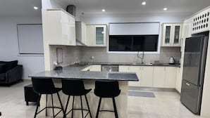 A modern kitchen with a central island, bar stools, a refrigerator, and a dining area with a sofa.