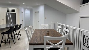 A modern kitchen with white cabinetry, a wooden dining table, and black bar stools.