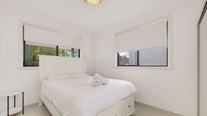 A white bedroom with a bed, a bedside table, and a window.