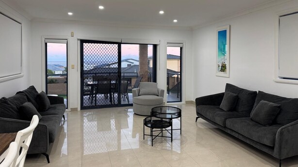 A spacious living room with two grey sofas, a small round table, and a sliding glass door leading to an outdoor patio.