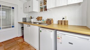 A kitchen with white cabinets, a wooden countertop, a sink, a toaster, and a refrigerator.