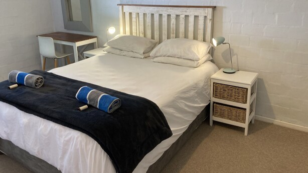 A neatly made bed with a headboard, a bedside table with a lamp, a chair, and a small table with a lamp.
