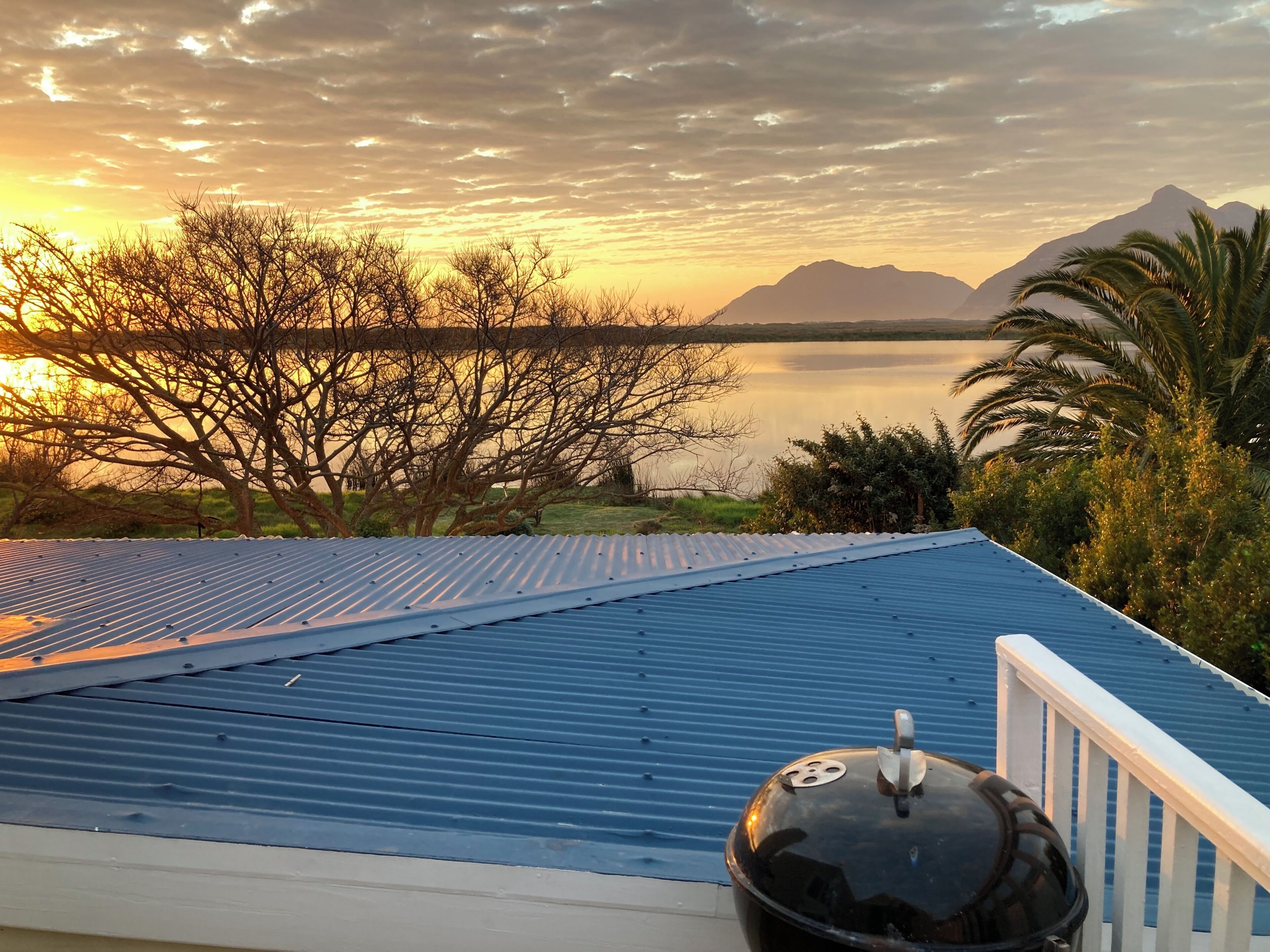 A rooftop with a blue metal roof, a black grill, and a white railing.