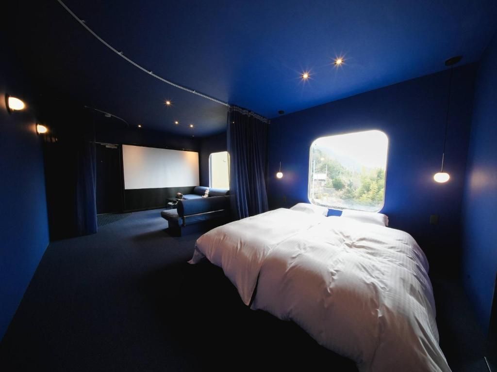 Una habitación con cama, un ventanal amplio, una pantalla de proyección y una zona de estar.