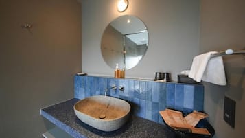 Un baño con un espejo redondo, un lavabo de piedra y un perchero para toallas.