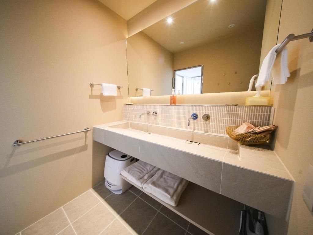 A modern bathroom with a large mirror, a towel rack, a sink with a soap dispenser, and a trash bin.