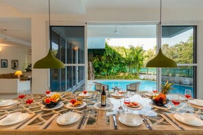 Un comedor con vista a la piscina, amplias ventanas y un jardín tropical.