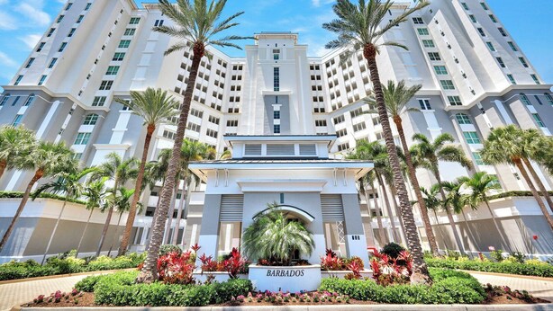 A multi-story hotel with a central entrance, palm trees, and a sign reading 'BARBADOS'. - Barbados at the Dunes (Naples)