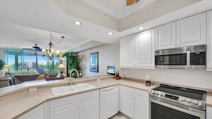 A modern kitchen with white cabinets, stainless steel appliances, and a large island with a sink. - Barbados at the Dunes (Naples)