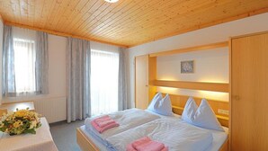 A double bed with pillows, a bedside table with a vase of flowers, and a wooden headboard. - Cozy Holiday Apartment With Balcony Near ski Slope (Maria Alm am Steinernen Meer)