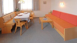 A room with a dining table, chairs, a sofa, and a small table with a lamp. - Cozy Holiday Apartment With Balcony Near ski Slope (Maria Alm am Steinernen Meer)