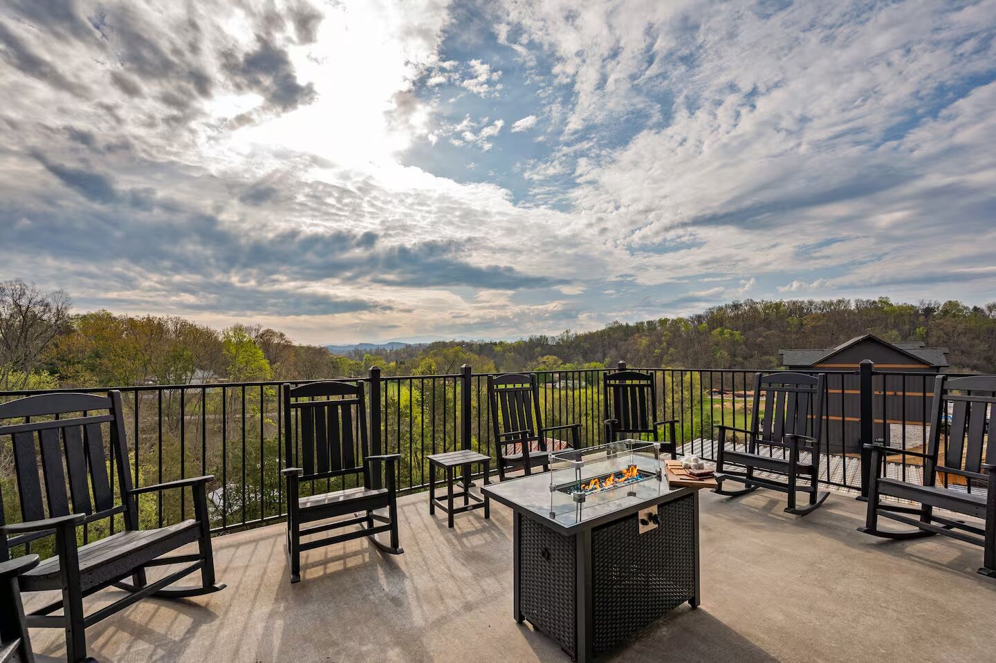 Una terraza con mobiliario exterior, una mesa con cubierta de vidrio y un hogar, con vista a un paisaje boscoso.
