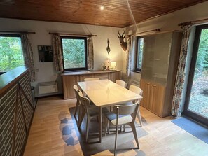 A dining area with a wooden table and chairs, a kitchen area with a window, and a deer head decoration on the wall. - Charming Holiday Base in the Ardennes for 8 (Rendeux)