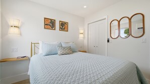 A bedroom with a bed, bedside lamps, a door, and wall-mounted artwork. - Pelican's Perch Cottage - New & Modern In Perfect Location w/ Waterfront Deck (St. Augustine)